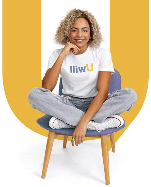 a woman with medium toned skin and blonde curly hair is wearing a white tshirt with the word Uwill on it. She is sitting on a chair and smiling.